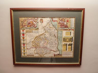 A framed historical map with illustrations and coats of arms on a wall at Glencoe House in Wooler