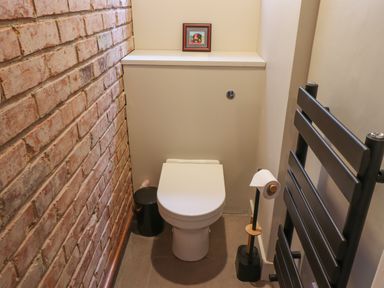 A small bathroom with a white toilet a black towel radiator and a brick wall at Glencoe House in Wooler