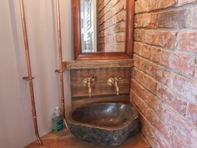 A bathroom sink with brass taps and a wooden framed mirror on a brick wall at Glencoe House in Wooler
