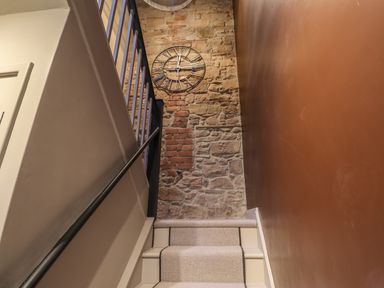 A staircase with carpeted steps and a stone wall featuring a clock at Glencoe House in Wooler
