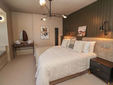 A bedroom with a large bed with pillows bedside tables a dressing table with towels and wall art at Glencoe House in Wooler