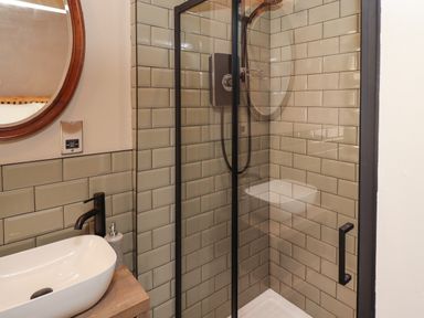 A bathroom with a glass shower enclosure a white sink with black faucet and a round mirror at Glencoe House in Wooler