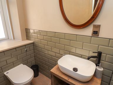A bathroom with a toilet sink mirror and green tiled walls at Glencoe House in Wooler