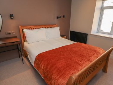 A bedroom with a wooden bed and red blanket next to a desk and window at Glencoe House in Wooler