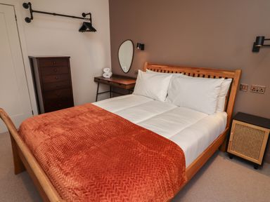 A bedroom with a wooden bed with white bedding and an orange blanket a dark wooden chest of drawers a small desk with a mirror and towels and a bedside table at Glencoe House in Wooler