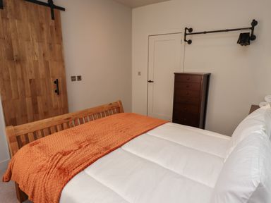 A bedroom with a bed covered with white bedding and an orange blanket a wooden chest of drawers and a wooden sliding door at Glencoe House in Wooler