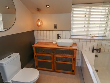 A bathroom with a toilet wooden vanity with a sink bathtub and window blinds at Glencoe House in Wooler