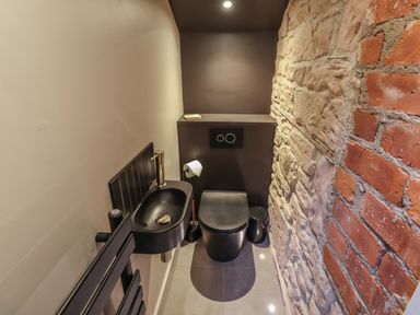 A small bathroom with a black toilet and sink next to a brick and stone wall at Glencoe House in Wooler