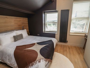 A bedroom with a bed white bedding throw pillows two windows and wooden floor at Glencoe House in Wooler