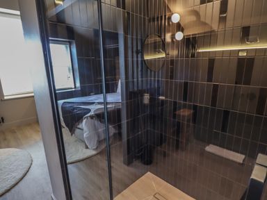A bedroom with a window and a bed reflected in a tiled shower enclosure at Glencoe House in Wooler