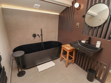 A bathroom with a black bathtub a wooden stool a black sink and a round mirror at Glencoe House in Wooler