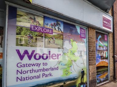 A street view of a building wall with a large promotional poster for Wooler and Northumberland National Park in Wooler