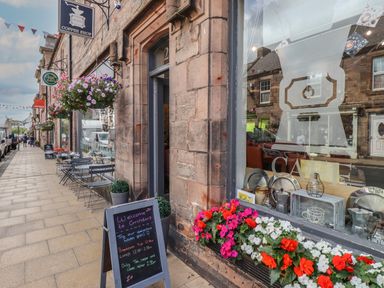 A coffee shop exterior with outdoor seating and flower baskets on a sidewalk at Glencoe House in Wooler