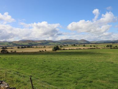 A green field with a wire fence and hills in the background under a sky with clouds at Glencoe House in Wooler
