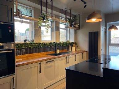 A kitchen with wooden countertops plants above the sink and black island at Glencoe House in Wooler
