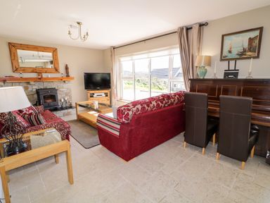 A living room with a stone fireplace a television red sofas a wooden piano and large windows at Inverbeg Cottage 1 in Downings