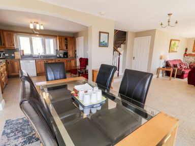 A dining area with a glass table and black chairs next to a kitchen with wooden cabinets and a living room with red sofas at Inverbeg Cottage 1 in Downings