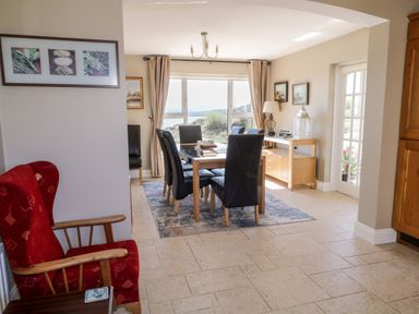 A dining room with a wooden table and black chairs near large windows next to a red armchair at Inverbeg Cottage 1 in Downings