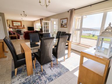 A dining room with a glass table and black chairs next to a large window overlooking water at Inverbeg Cottage 1 in Downings