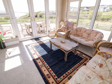 A sunlit seating area with wicker furniture and a rug near glass doors overlooking an outdoor patio at Inverbeg Cottage 1 in Downings