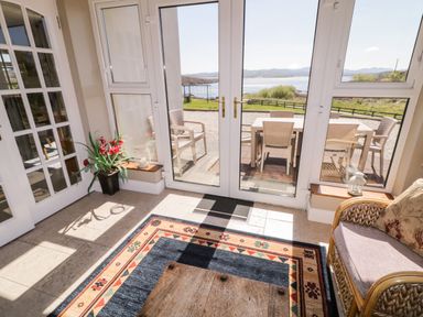 A sitting area with a woven chair cushion and a coffee table near glass doors leading to an outdoor dining set and water view at Inverbeg Cottage 1 in Downings