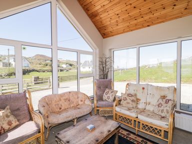 A seating area with wicker sofas and armchairs around a wooden coffee table in a room with large windows at Inverbeg Cottage 1 in Downings