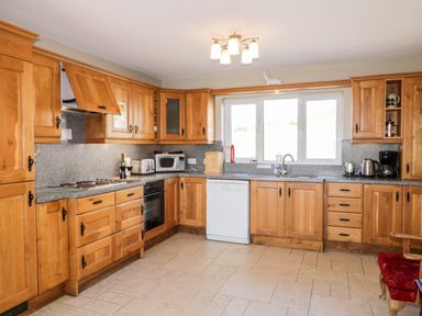 A kitchen with wooden cabinets a dishwasher microwave oven toaster and coffee maker at Inverbeg Cottage 1 in Downings