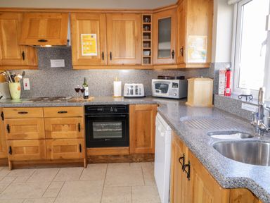 A kitchen with wooden cabinets, a countertop, an oven, a microwave, a toaster, and a sink at Inverbeg Cottage 1 in Downings