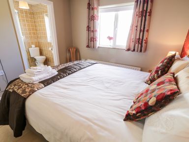 A bedroom with a bed with pillows and folded towels next to a window and an adjoining bathroom at Inverbeg Cottage 1 in Downings