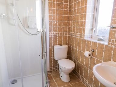 A bathroom with a shower enclosure toilet and sink with tiled walls and a window at Inverbeg Cottage 1 in Downings