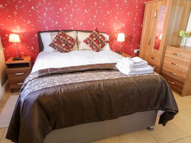 A bedroom with a double bed two patterned cushions nightstands lamps wooden wardrobe and dresser at Inverbeg Cottage 1 in Downings