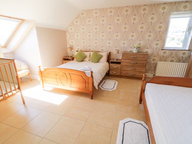 A bedroom with two wooden beds a wooden chest of drawers two bedside tables with lamps and a chair at Inverbeg Cottage 1 in Downings