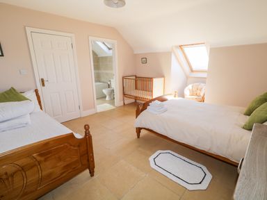 A bedroom with two wooden beds a crib a chair a small rug and an en suite bathroom at Inverbeg Cottage 1 in Downings