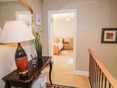 A hallway with a table lamp and plant next to a mirror leading to a bedroom with a bed and wooden furniture at Inverbeg Cottage 1 in Downings