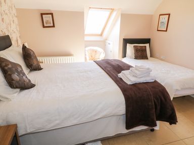A bedroom with a double bed and a single bed with folded towels on the double bed at Inverbeg Cottage 1 in Downings