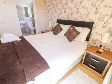 A bedroom with a double bed pillows bedside tables lamps and an en suite bathroom at Inverbeg Cottage 1 in Downings