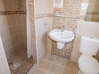 A bathroom with a shower area a wall-mounted sink a toilet and tiled walls at Inverbeg Cottage 1 in Downings