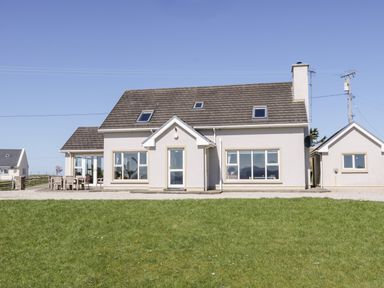 A two story house with large windows and a patio set outside on a lawn at Inverbeg Cottage 1 in Downings