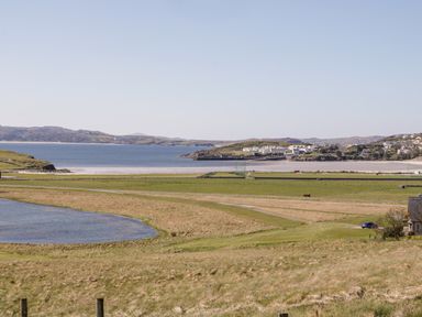 A coastal landscape with grassy fields a small pond and buildings near the shore at Inverbeg Cottage 1 in Downings