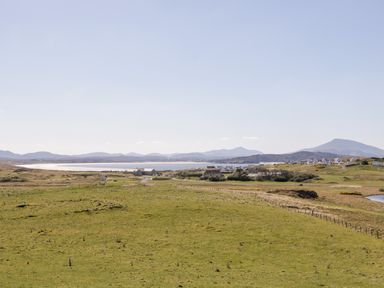 A grassy field with a fence and houses near a body of water with mountains in the background at Inverbeg Cottage 1 in Downings