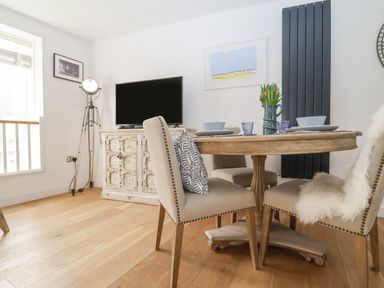 A dining area with a round wooden table set with dishes and a vase of flowers and beige chairs at The Gallivant in Southwold