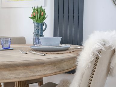 A dining table with plates fork glasses and a vase with tulips with a chair draped with a white fur at The Gallivant in Southwold