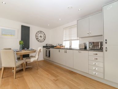 A kitchen with dining table set with tulips clock on wall and cabinets at The Gallivant in Southwold