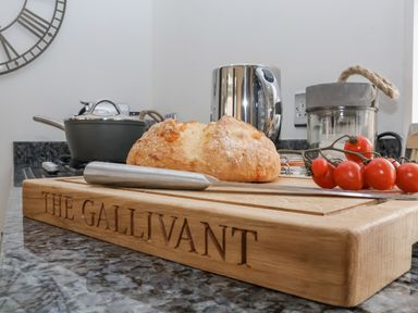 A kitchen counter with a chopping board inscribed The Gallivant holding bread a knife and tomatoes at The Gallivant in Southwold