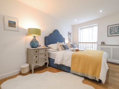 A bedroom with a blue upholstered bed yellow throw and a bedside table with a lamp at The Gallivant in Southwold