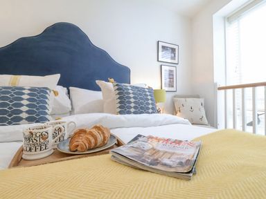 A bedroom with a blue headboard croissants on a tray and magazines on a yellow blanket at The Gallivant in Southwold