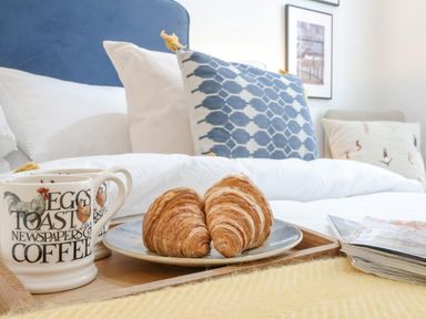 A bedroom with a wooden tray holding croissants and coffee mugs on a bed with pillows at The Gallivant in Southwold