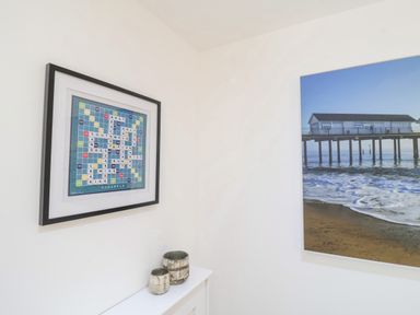 A corner wall with a framed Scrabble board and a framed photograph of a pier over water at The Gallivant in Southwold