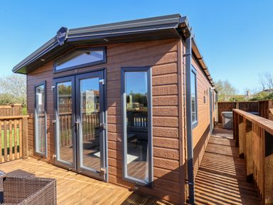 Exterior view of a wooden lodge with large windows and a deck area at Mayflower Lodge in Runswick Bay near Staithes