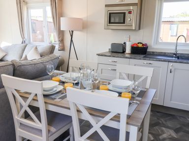 A kitchen and dining area with a table set for four and a sofa in the background at Mayflower Lodge in Runswick Bay near Staithes